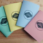 Four Pastel coloured notebooks with the SRUCSA logo